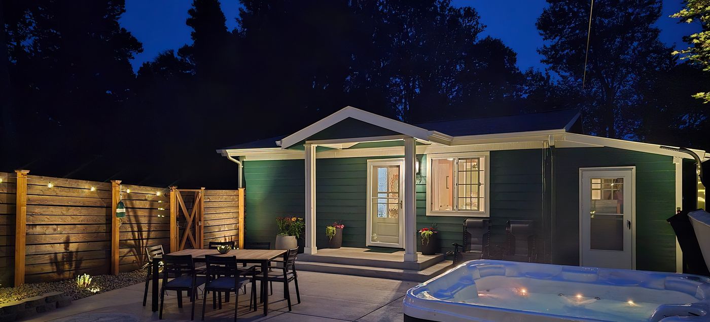 The Resthouse exterior at dusk, porch lit with the dining area and hot tub in view